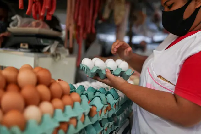 Mulher ao lado de diversas cartelas com ovos brancos e vermelhos