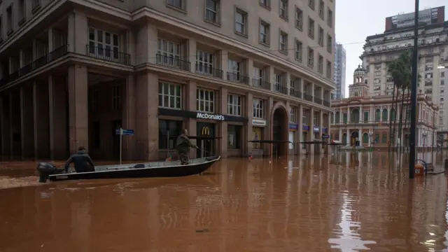 Imagem mostra dois homens usando barco para percorrer ruas de Porto Alegre