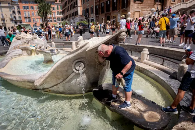 Um homem se refresca em uma fonte de água para escapar do calor