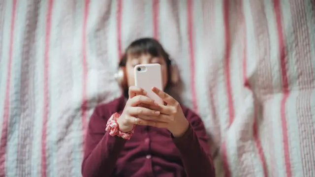 Foto vista do alto, com uma adolescente segurando um celular em frente ao rosto 