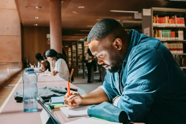 Homem fazendo anotação no caderno em biblioteca