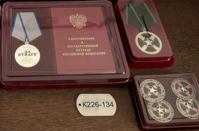 Uma placa de identificação com a inscrição 'K226-134', ao lado de uma medalha gravada com as palavras 'por bravura'