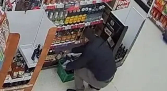 Homem colocando garrafas em cesta de supermercado