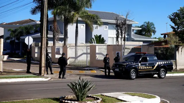 Viatura e policiais em frente a casa em dia ensolarado