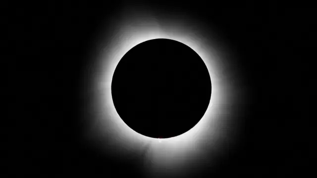 Foto em preto e branco mostra o Sol completamente encoberto pela lua. Só é possível ver o brilho branco do sol, que irradia por volta da circunferência formada pela lua