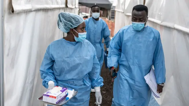 Trabalhadores da saúde usando máscaras e aventais conversam enquanto caminham entre as tendas no centro de tratamento de mpox em Munigi, no Congo, em 17 de agosto