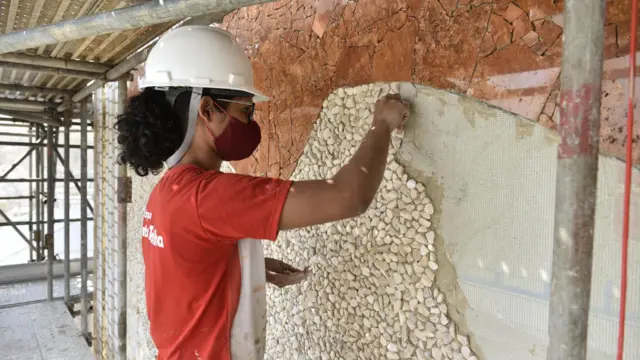 Mulher trabalha montando mosaico em parede