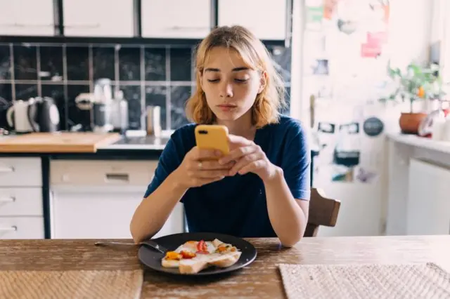 yemek yerken telefonuna bakan bir kadın