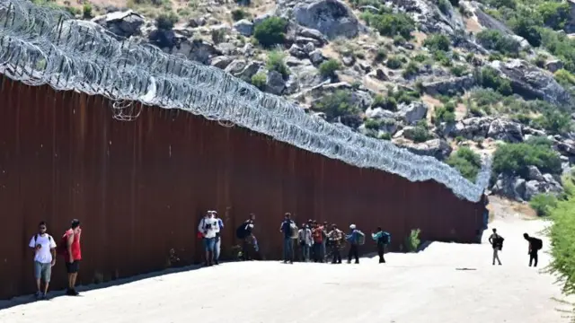 Migrantes entram nos EUA ao lado do muro da fronteira EUA-México em Jacumba Hot Springs, Califórnia, junho de 2024