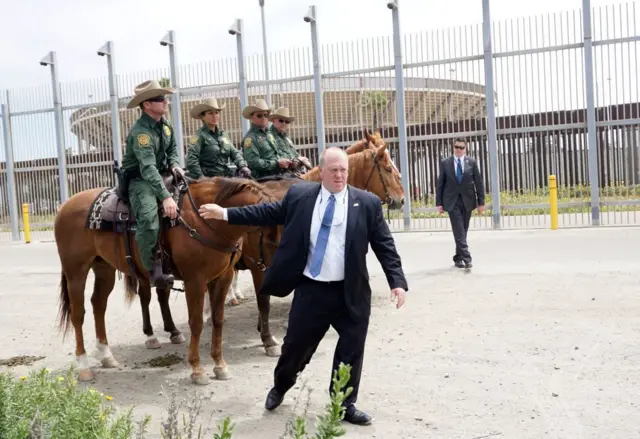 Tom Homan perto de policiais em cavalos, perto de grade