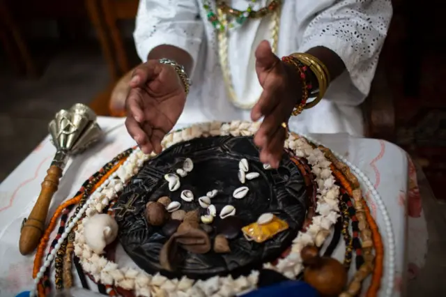 Pessoa com trajes típicos jogando búzios