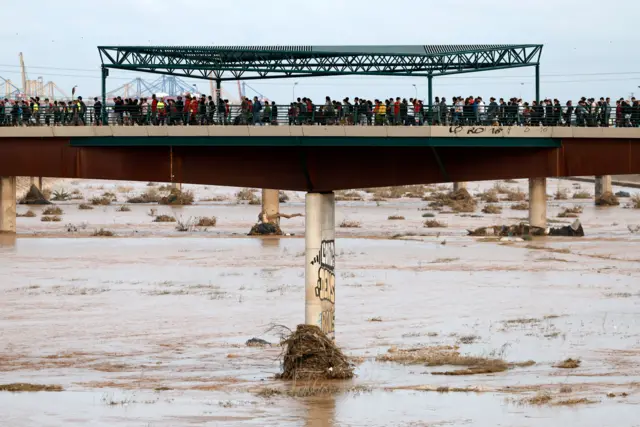 Dezenas de pessoas cruzando ponte sobre rio