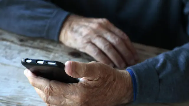 mão de um homem idoso segurando um celular 