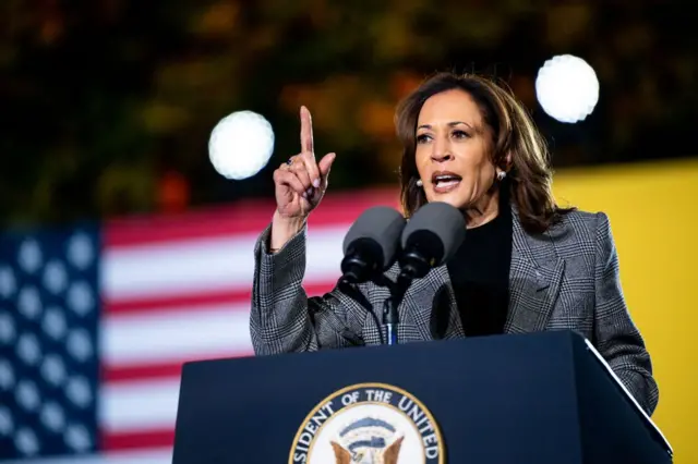 Kamala Harris discursando em palanque, com bandeira dos EUA ao fundo