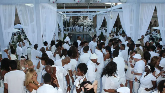 Dezenas de pessoas vestidas de branco reunidas ao redor de uma piscina com lustres de brilhantes e cortinas brancas transparentes na 'Festa do Branco' de Sean 'Diddy' Combs em 2007