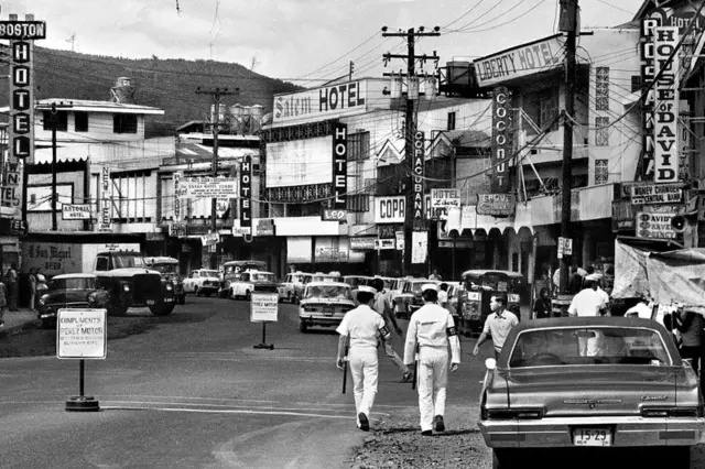 Dois oficiais de patrulha costeira da Marinha dos EUA caminham por Olongapo, uma cidade nas Filipinas frequentemente chamada de cidade de Olongapo. Olongapo era um destino popular para os marinheiros da Marinha dos EUA estacionados na adjacente Base Naval dos EUA Subic Bay.