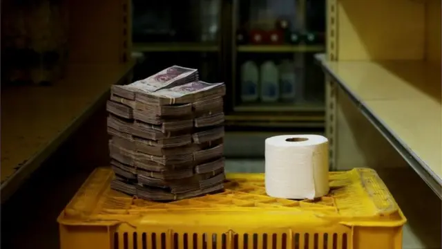 Pilha de notas de bolívares ao lado de rolo de papel higiênico