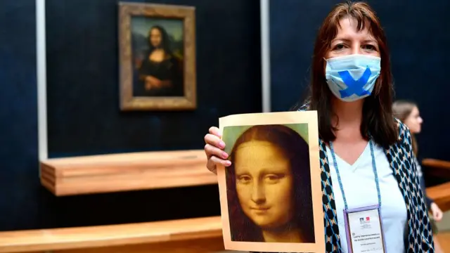 Mulher segurando um cartaz da Mona Lisa em frente ao quadro no Museu do Louvre