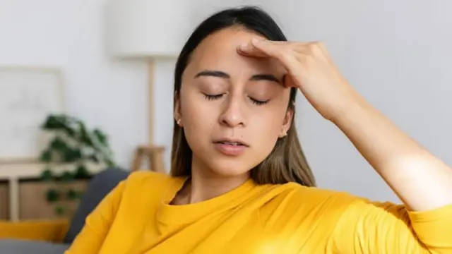 Mulher de pele clara e cabelo liso comprido coloca a mão nas têmporas