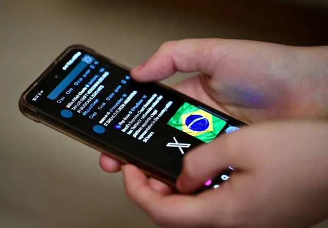 Pessoa segurando celular, com aplicativo do Twitter aberto; na linha do tempo, é possível ver post com bandeira do Brasil