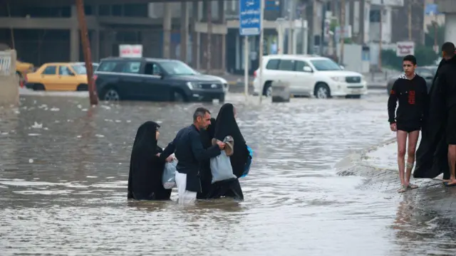 Pessoas caminham por ruas inundadas devido à infraestrutura precária após fortes chuvas em Najaf, Iraque, em 26 de março de 2023