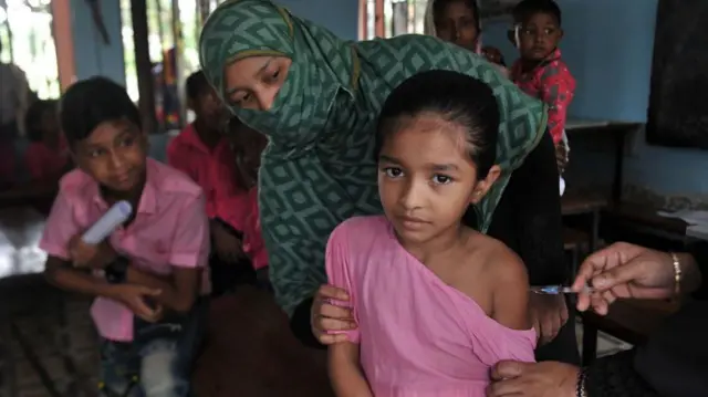 Uma menina com um vestido cor de rosa recebe uma vacina no braço 