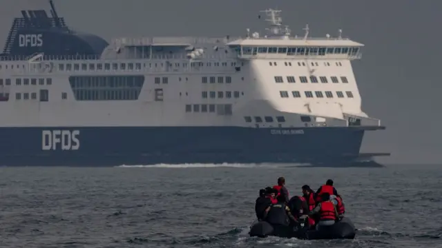 Barco cheio de imigrantes no Canal da Mancha ao lado de uma balsa