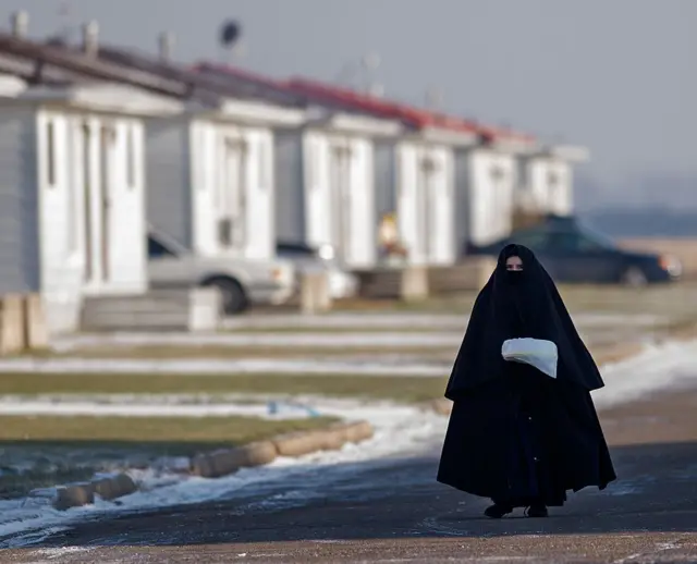 Membro da comunidade Lev Tahor, provavelmente uma mulher, completamente coberta da cabeça aos pés com vestimenta preta. Apenas seus olhos e testa são visíveis. Ela caminha por uma rua nevada.