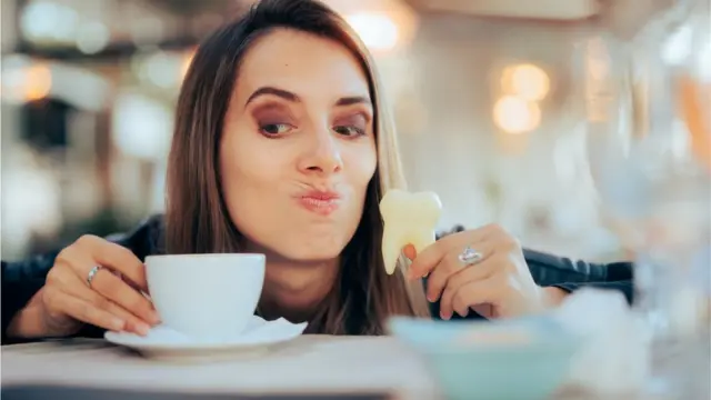 Mulher segurando xícara de café e escultura em formato de dente na outra