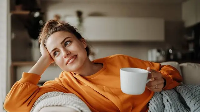 Mulher sorrindo tomando chá em sofá