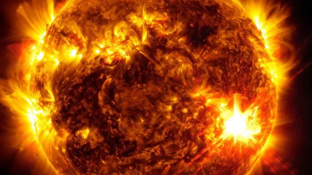 Ilustração mostrando a superfície do sol durante tempestade solar: há pontos mais claros e 'fios dourados' de explosões