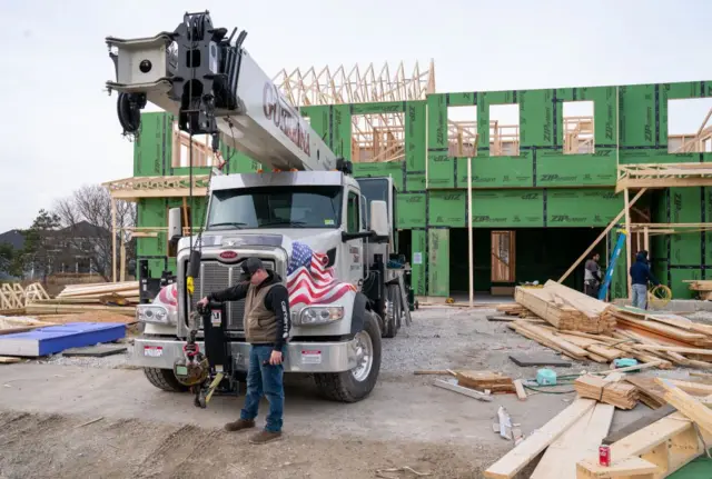 Casas sendo construídas, com caminhão e homem em frente a obra