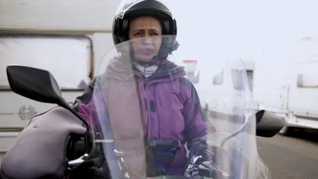 Célia Campos em sua moto, parada em frente ao trailer onde mora