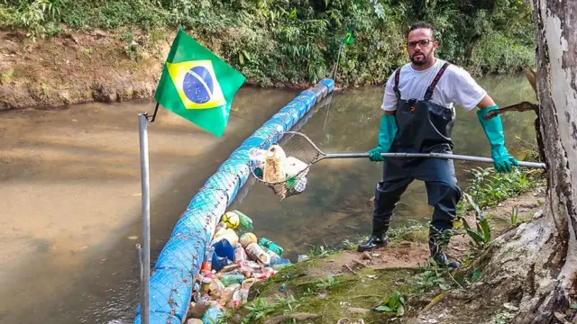 Diego em pé segurando uma rede cheia de lixo que retirou da barreira ecológica