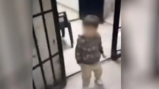 Uma criança pequena, com 3 ou 4 anos, passando pela porta aberta de uma cela em imagem capturada de vídeo