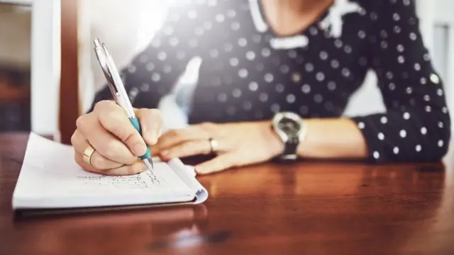 Mulher escrevendo em caderno sobre uma mesa