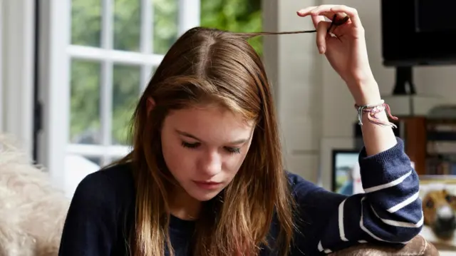 Uma menina enrolando uma mecha de cabelo enquanto olha para celular