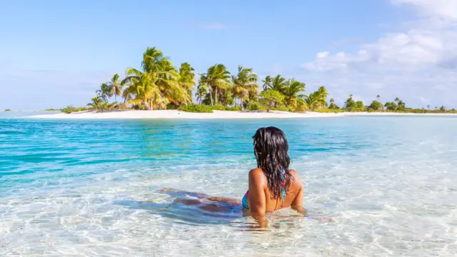 Uma mulhe sentada em um mar cristalino observando uma ilha idílica à distância