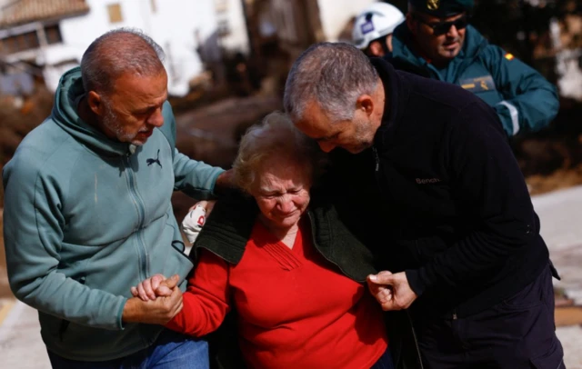 Idosos brancos ajudando uma idosa branca a andar durante enchente