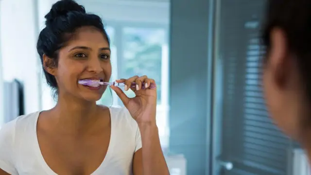 Mulher escovando dente em frente a espelho