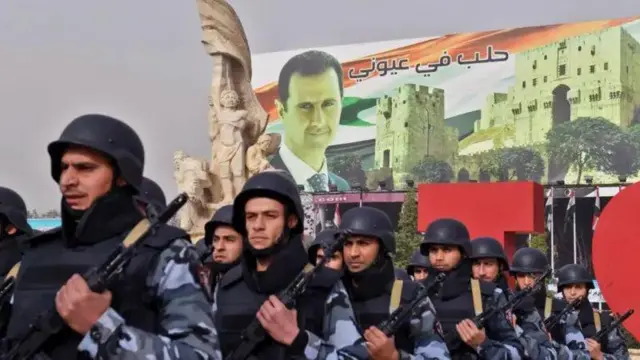 Imagem mostra uma fila de homens do exército com a foto de Bashar al-Assad ao fundo.