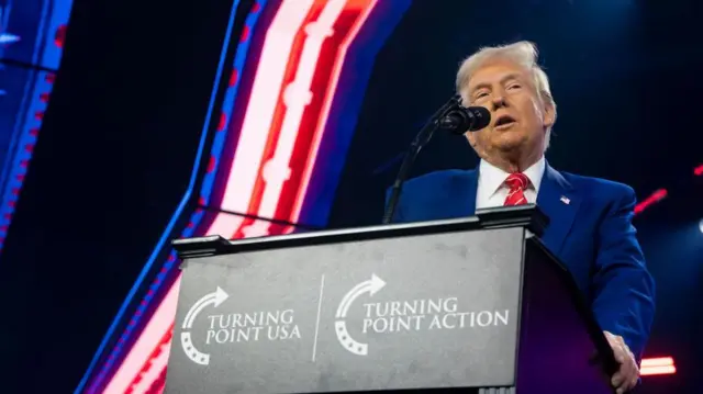 Donald Trump em frente a uma tribuna com o logotipo da Turning Point USA