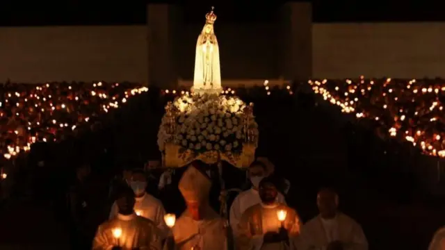 Pessoas caminhando com velas em mãos em procissão na Festa da Assunção