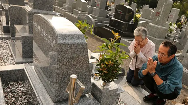 Um homem e uma mulher rezando na frente de um túmulo no Japão