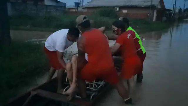 Bombeiros carregam idosa em barco durante alagamento