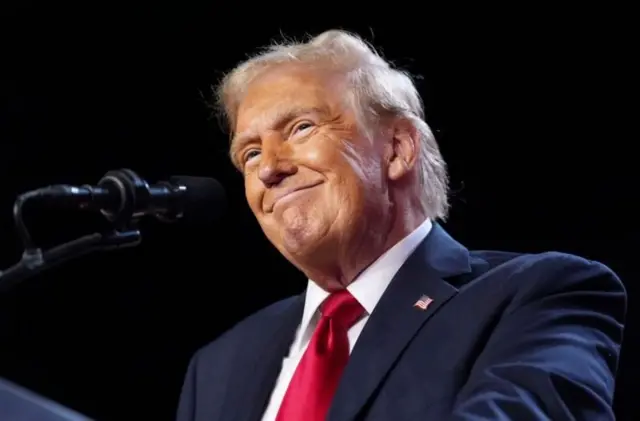 Trump sorrindo, próximo a microfone