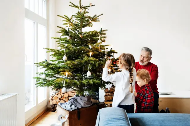 Um homem decorando uma árvore de Natal com duas crianças