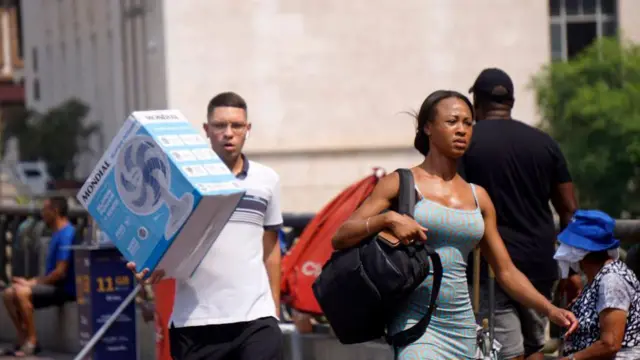 Homem andando com caixa de ventilador ao lado de mulher no centro de São Paulo