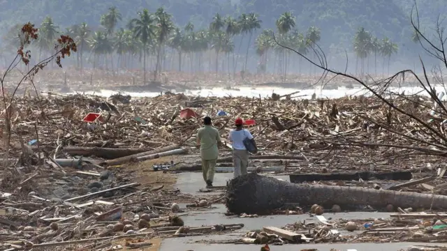 Dois homens caminham em meio à devastação causada pelo tsunami de 2004 na Indonésia