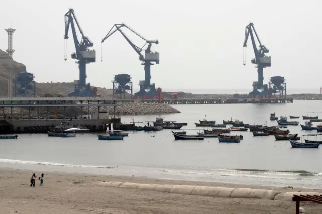 Pequenos barcos de pesca atracados na praia de Chancay, com o grande porto em construção ao fundo